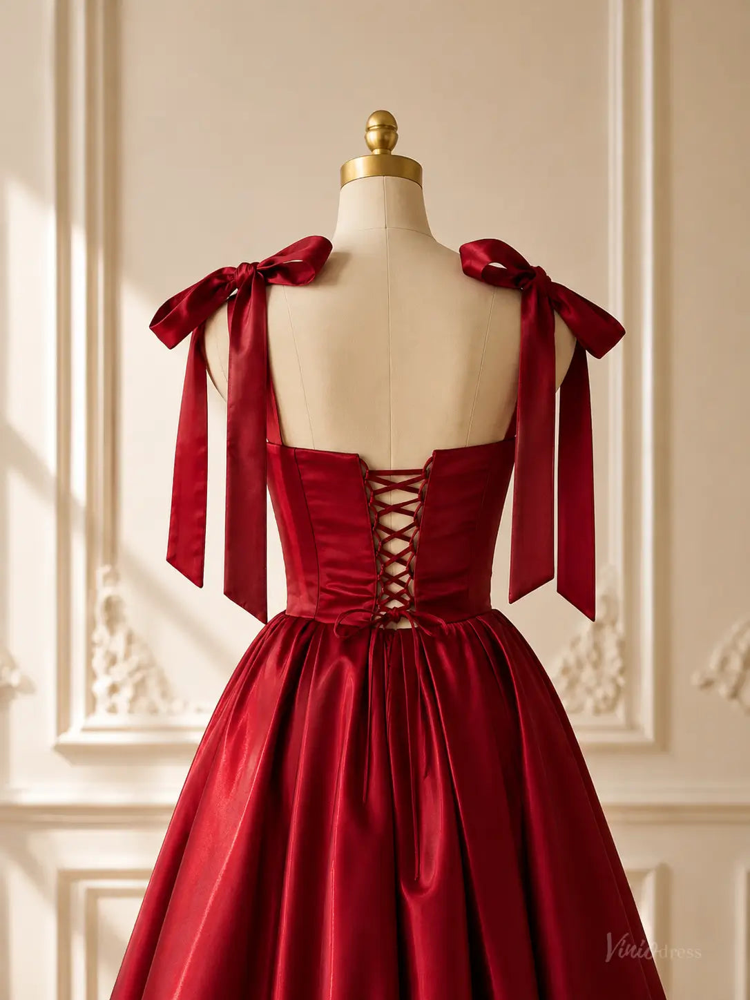 Burgundy satin ball gown with a lace-up corset back, bow shoulder straps, and a voluminous gathered skirt on a mannequin.