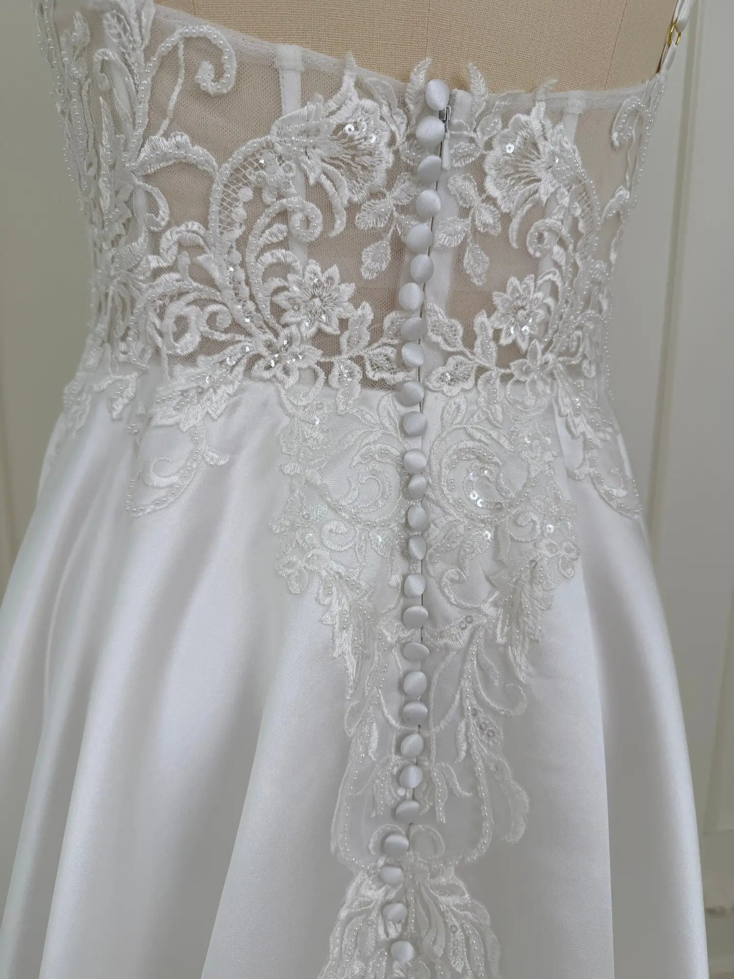 White satin wedding dress back with lace appliqué bodice and covered buttons.