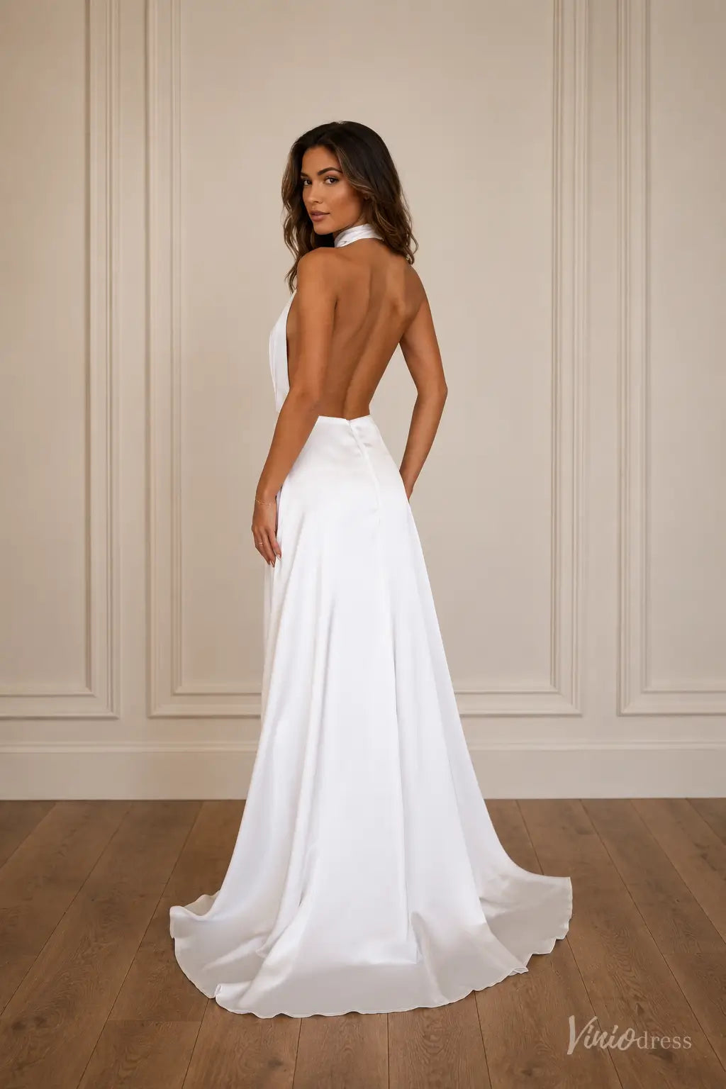 Minimalist white satin wedding dress with a halter neckline, plunging open back, and flowing A-line skirt.