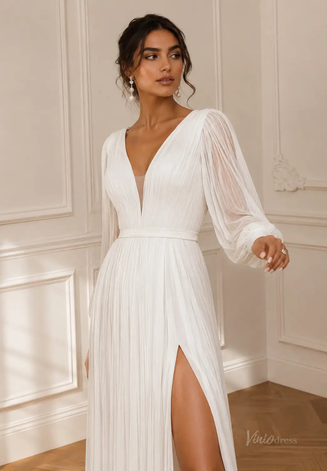 White pleated chiffon wedding dress with a deep V-neck, sheer long sleeves, and a high leg slit.