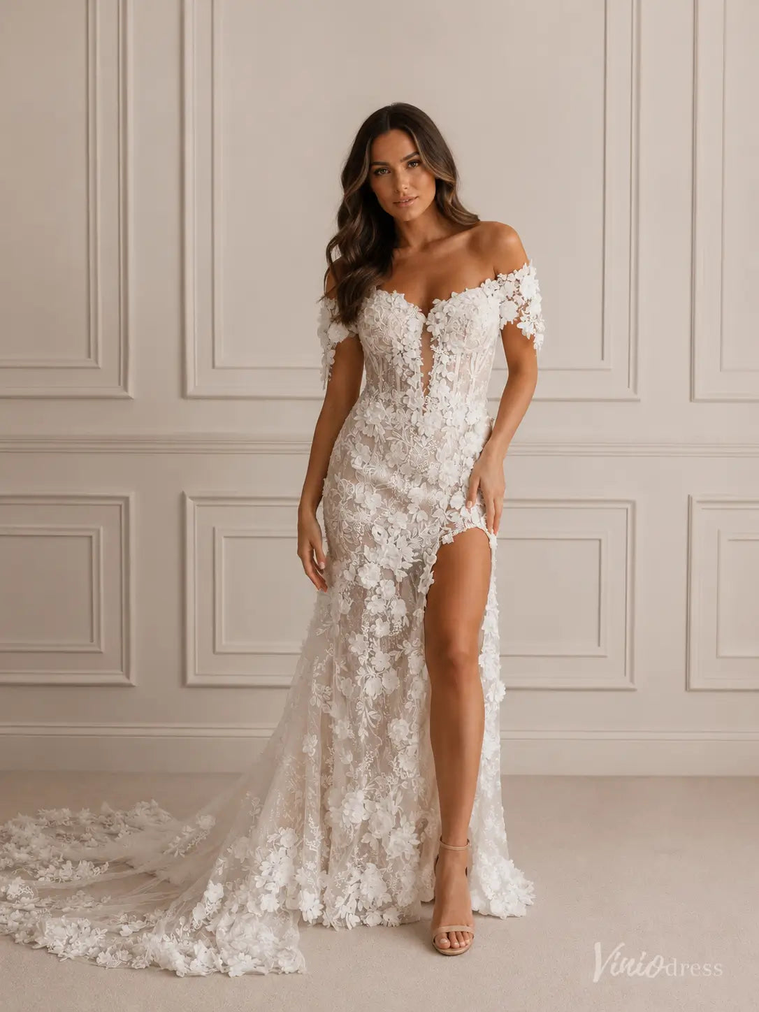Off-shoulder boho wedding dress with 3D floral appliqués, a plunging basque bodice, and a high-slit sheath skirt.
