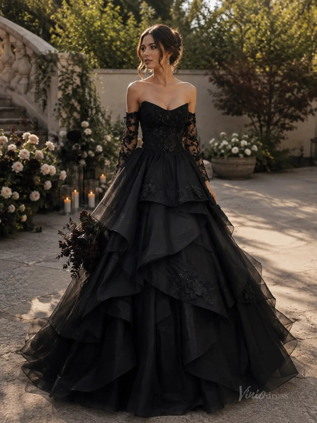 Black strapless ball gown with tiered tulle skirt, lace bodice, and matching long sleeves in a garden setting.