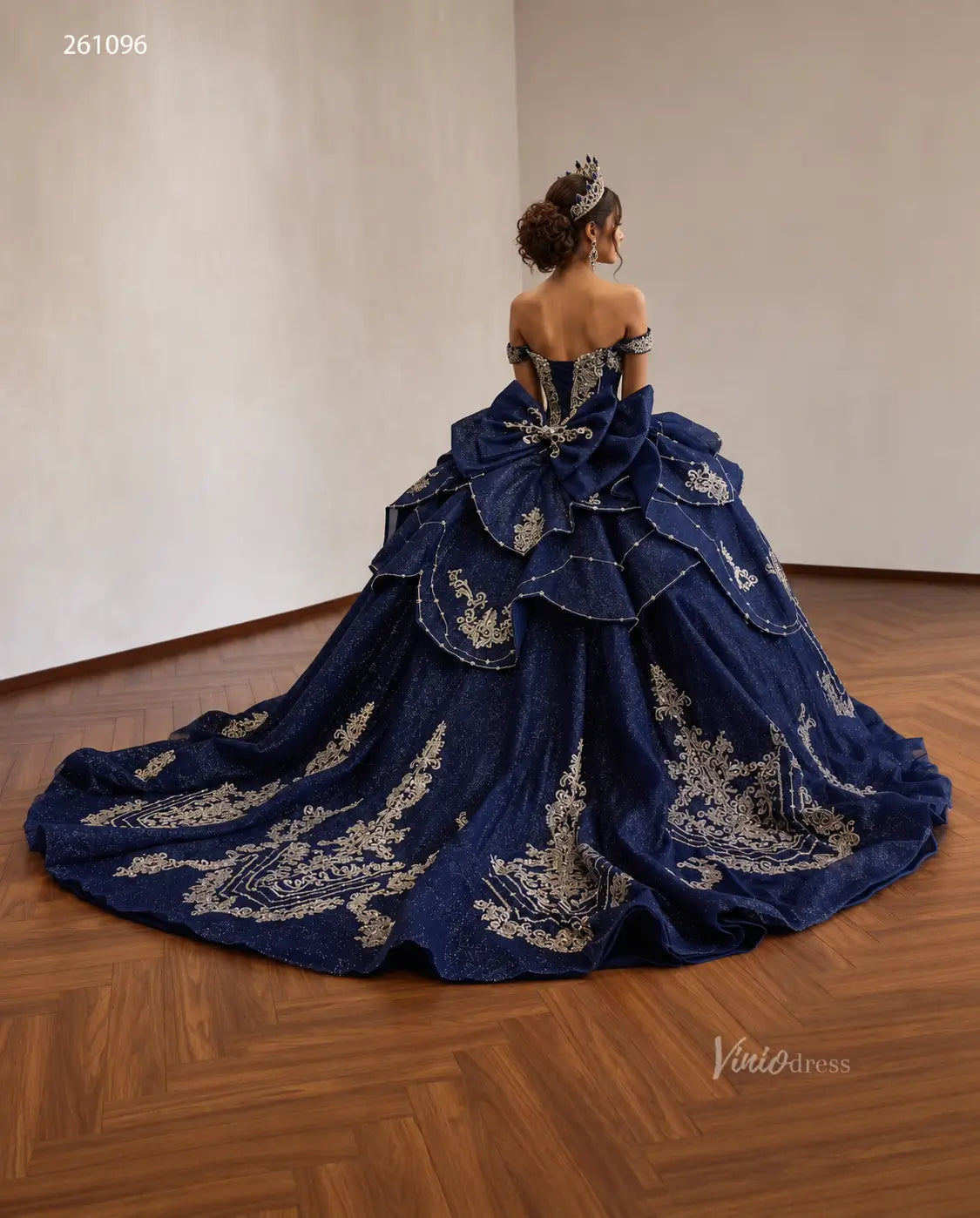 Navy blue quinceañera ball gown with gold baroque embroidery, tiered peplum, crystal corset, and oversized back bow.