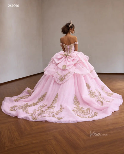 Pink off-shoulder quinceañera ball gown with gold baroque embroidery, crystal corset, tiered peplum, and oversized back bow.