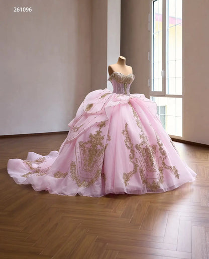 Pink off-shoulder quinceanera ball gown with gold baroque embroidery, crystal corset, and tiered peplum skirt.