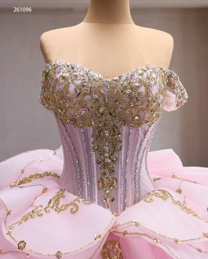 Pink quinceañera ball gown with gold baroque embroidery, crystal-encrusted corset bodice, and tiered peplum waist.