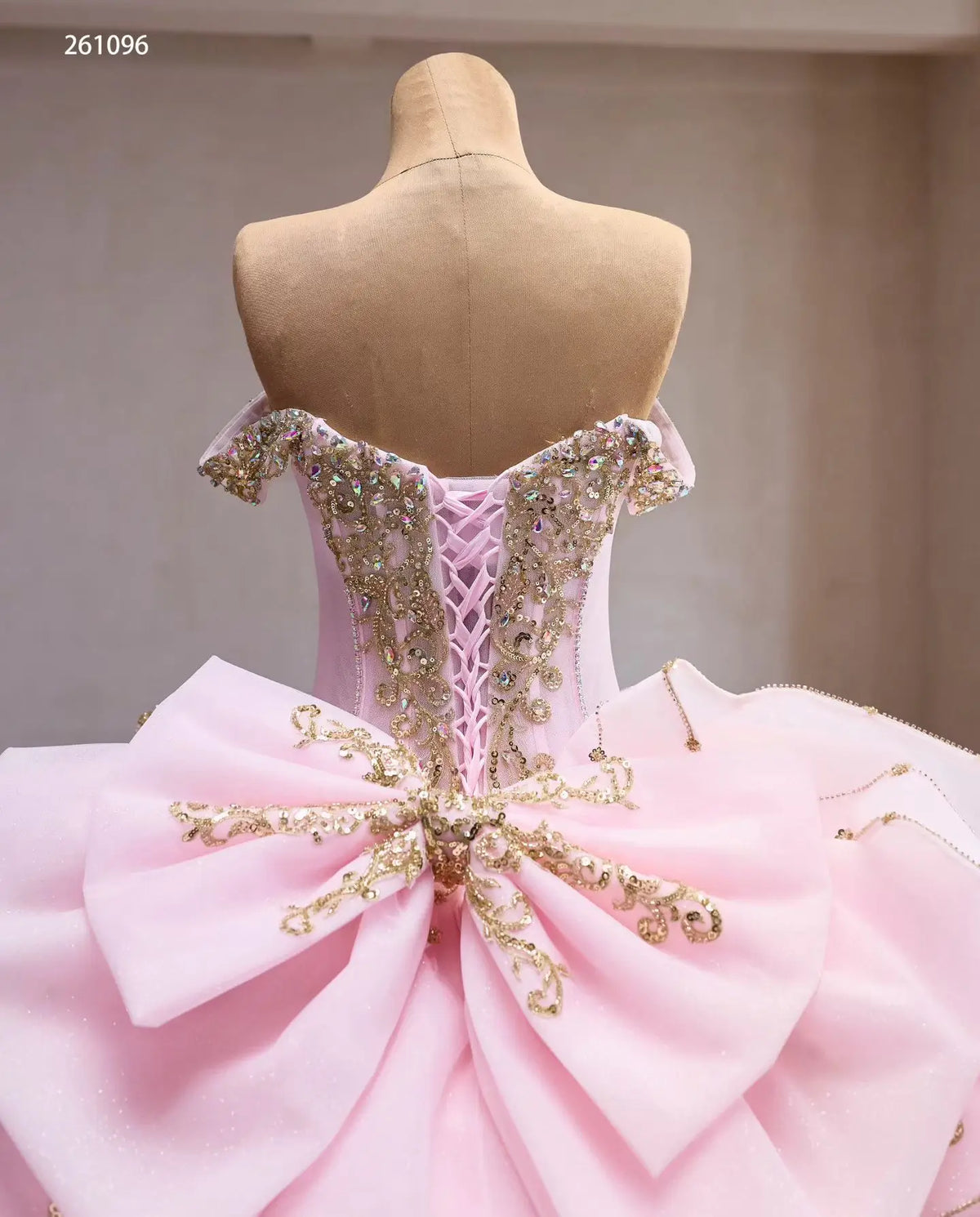 Pink off-shoulder quinceañera ball gown with gold baroque embroidery, crystal corset, lace-up back, and oversized bow.