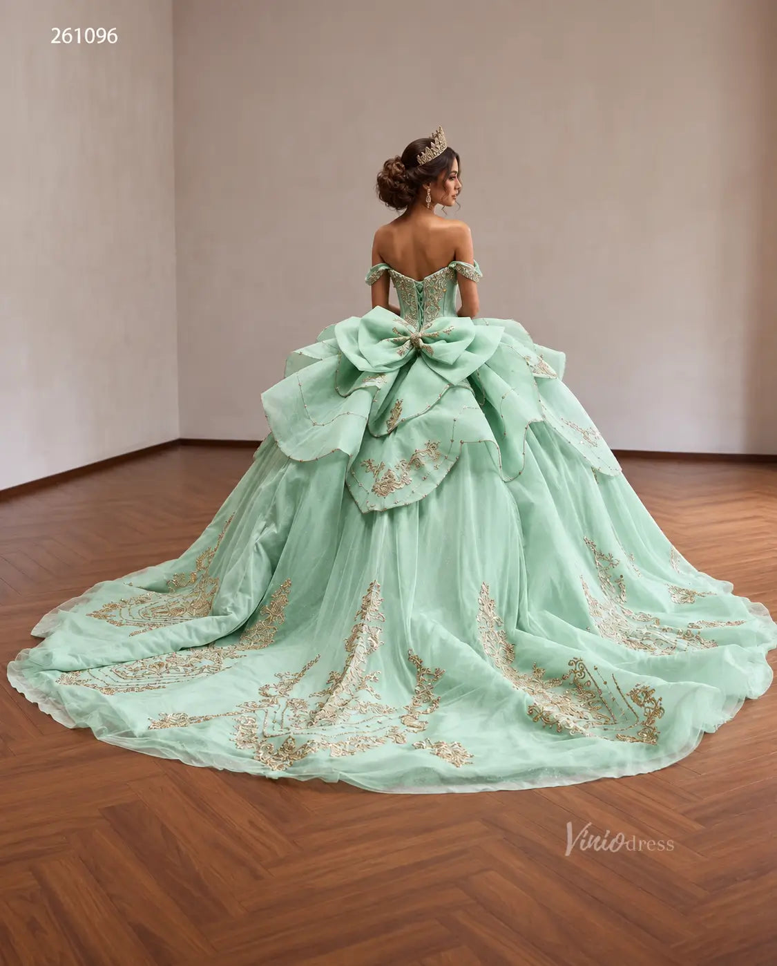 Mint green quinceañera ball gown with gold baroque embroidery, tiered peplum, and an oversized back bow.