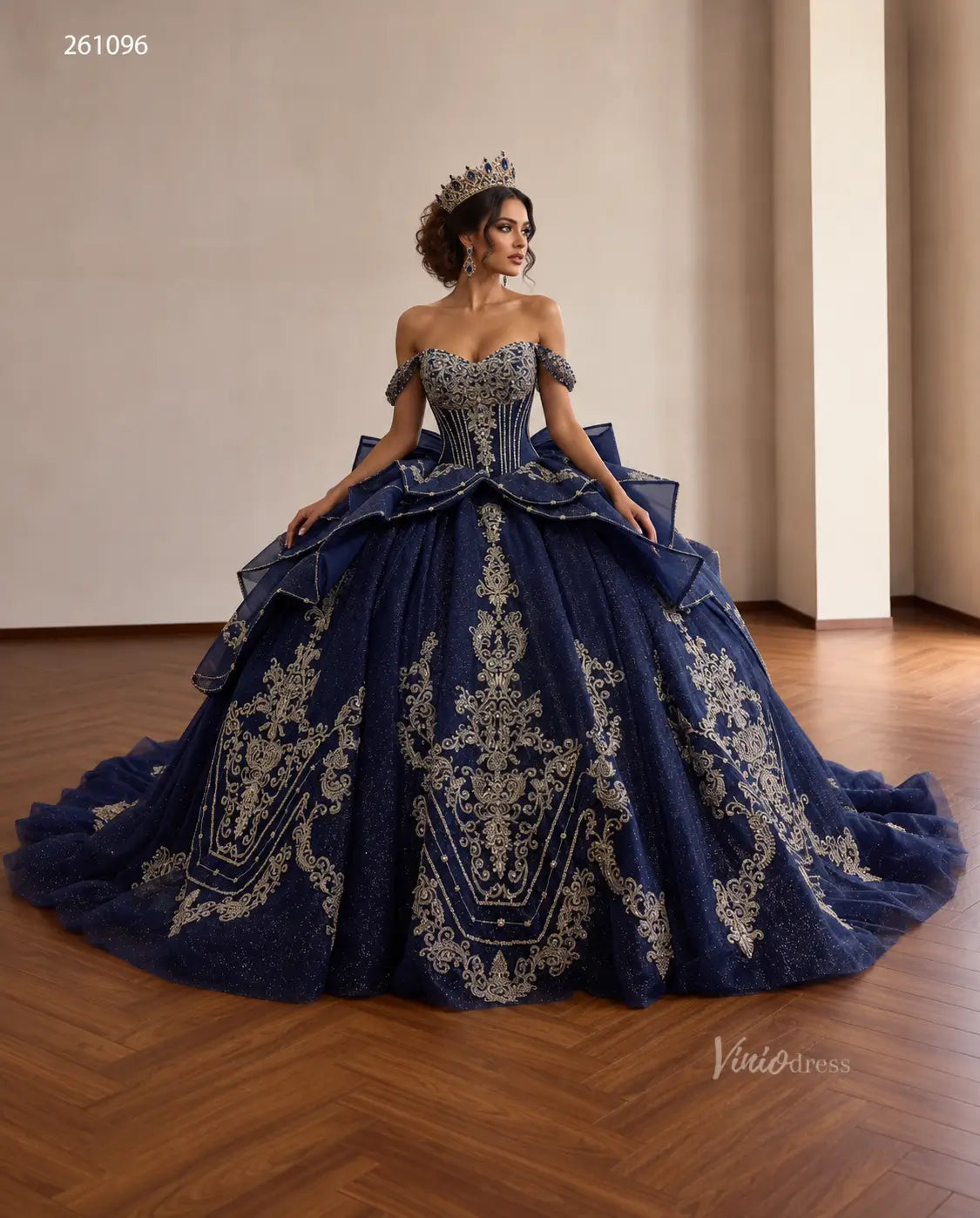Navy blue quinceañera ball gown with gold baroque embroidery, crystal corset, tiered peplum, and oversized back bow.