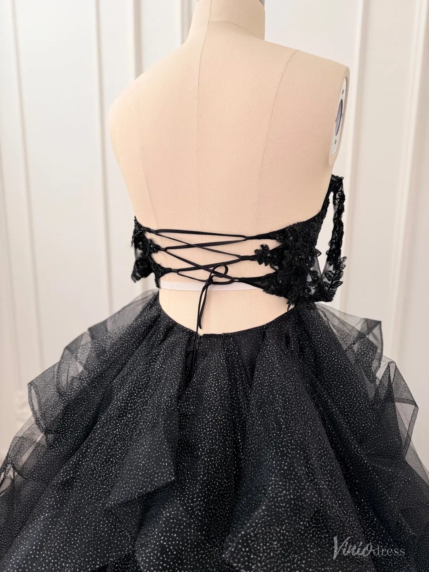Black glitter ball gown with lace appliqué, off-shoulder sleeves, and a corset back with lace-up closure on a mannequin.