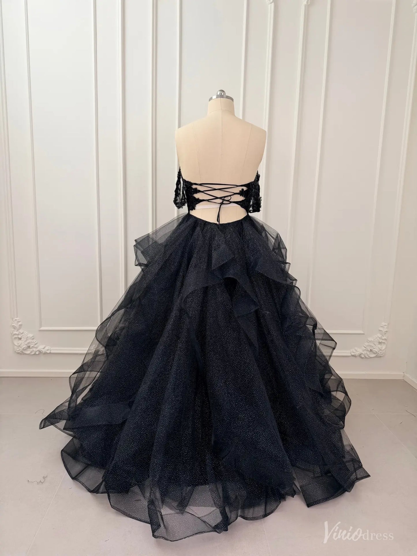 Black glitter tulle ball gown with off-shoulder sleeves, lace bodice, and a voluminous ruffled skirt on a mannequin.