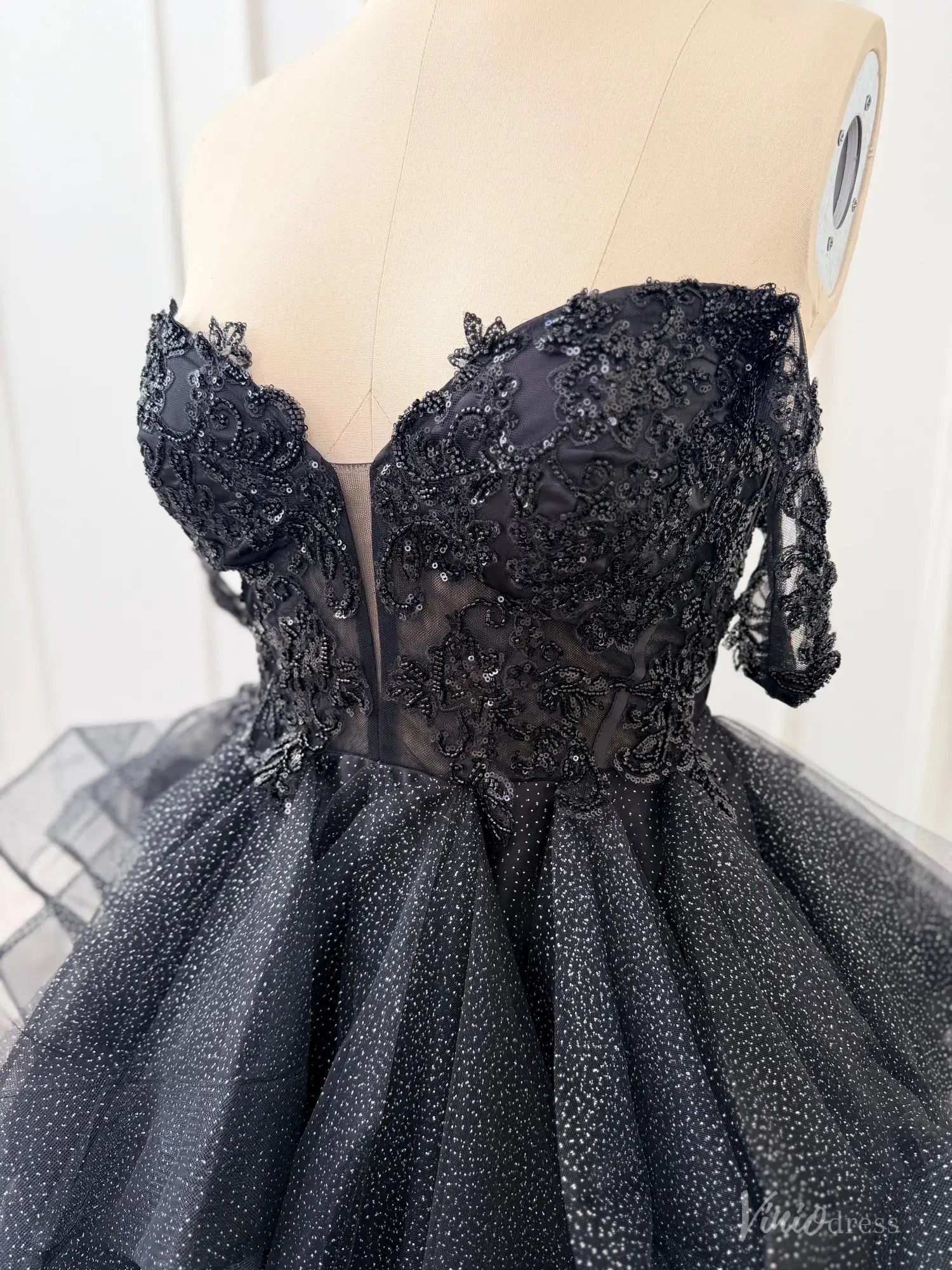 Black off-shoulder ball gown with a sequined lace corset bodice, illusion V-neck, and shimmering glitter tulle skirt.