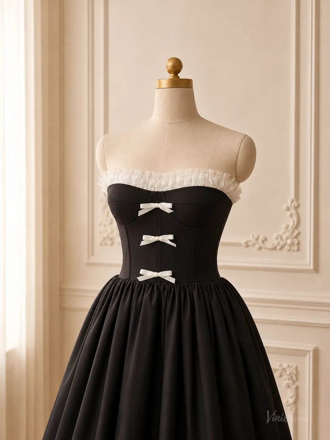 Black tea-length prom dress with a strapless corset bodice, white ruffle trim, and three delicate white bow details.