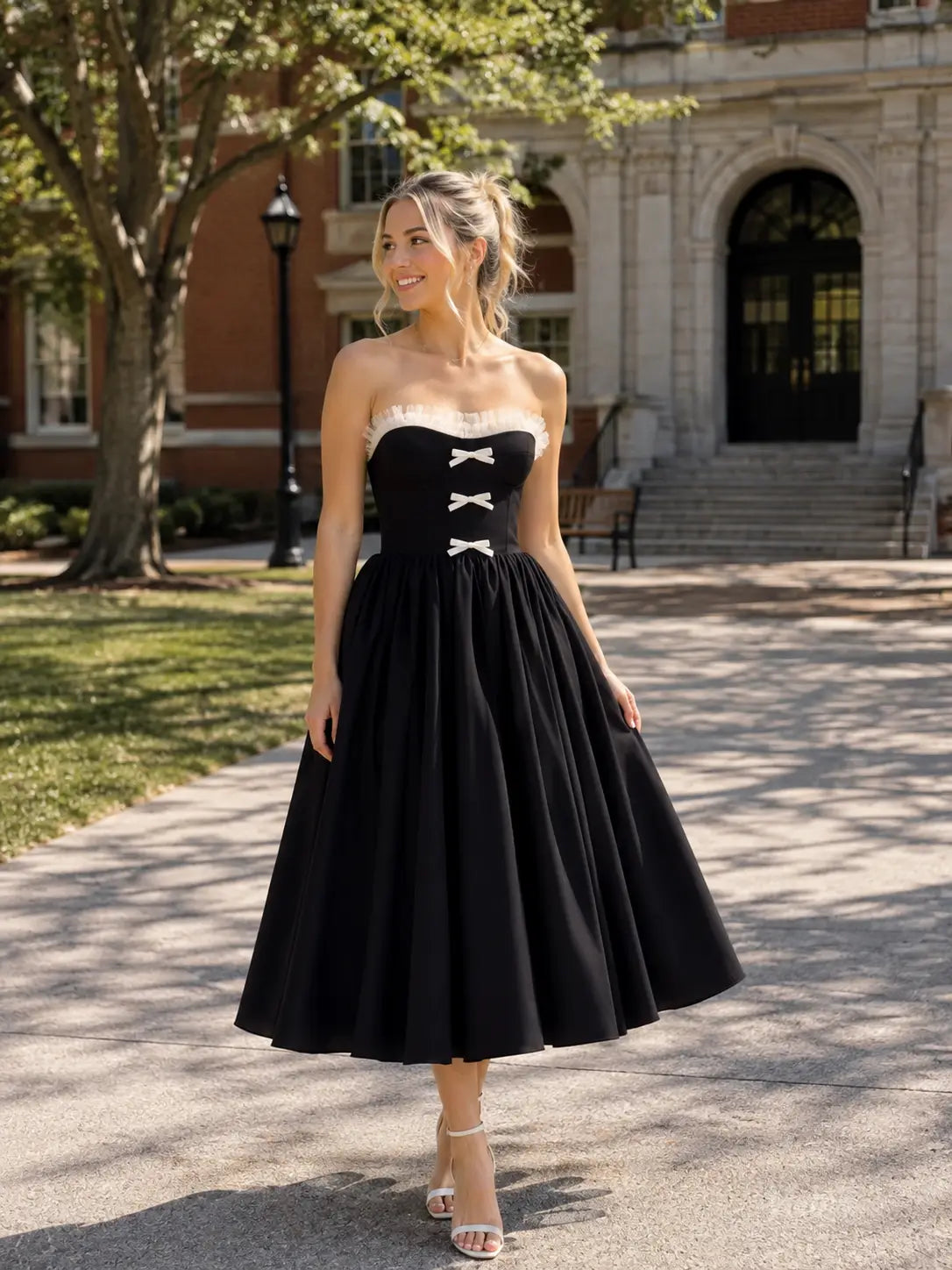 Black tea-length prom dress with a strapless corset bodice, white ruffle trim, and three front bows.