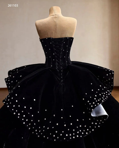 Black velvet quinceañera ball gown with crystal embellishments, lace-up corset back, and a ruffled peplum with silver lining.