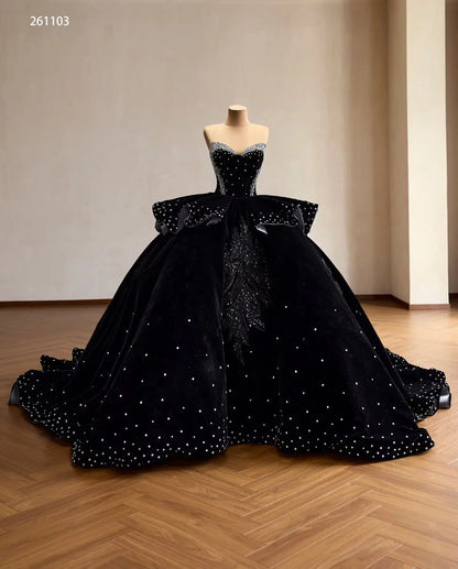 Black velvet quinceañera ball gown with crystal corset, ruffle peplum, and beaded leaf embroidery on a full skirt.