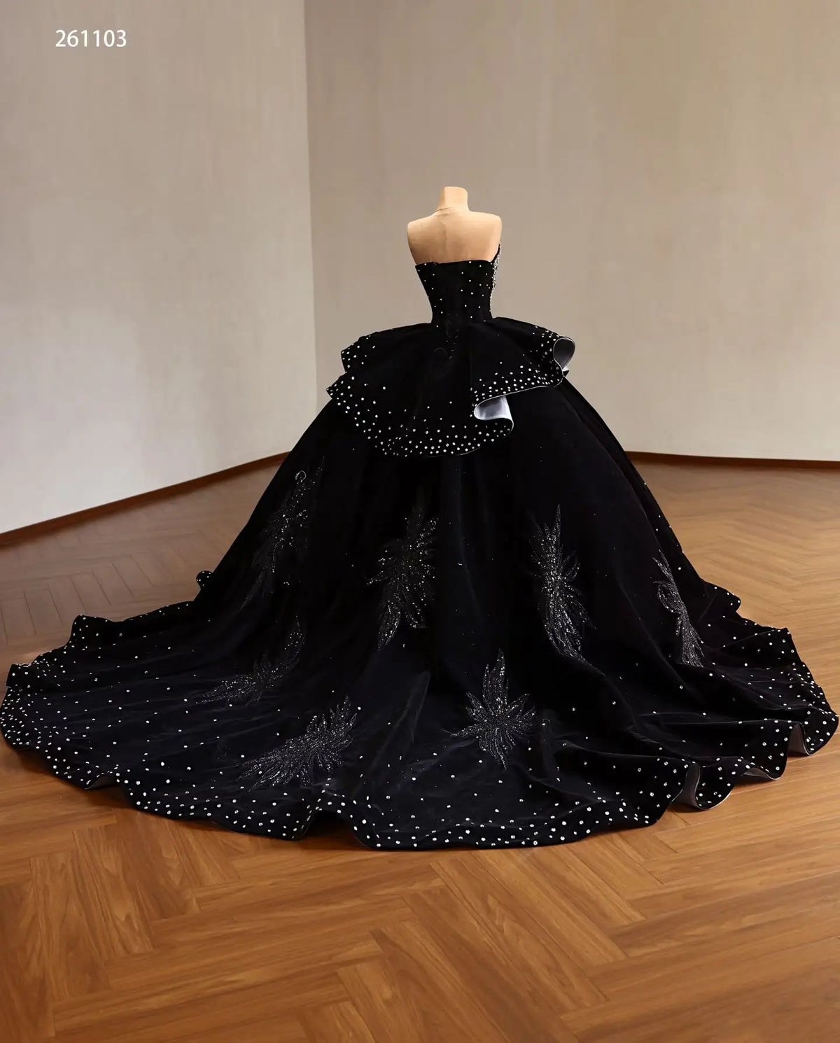Black velvet quinceañera ball gown with crystal accents, ruffle peplum, silver lining, and beaded leaf embroidery on a train.