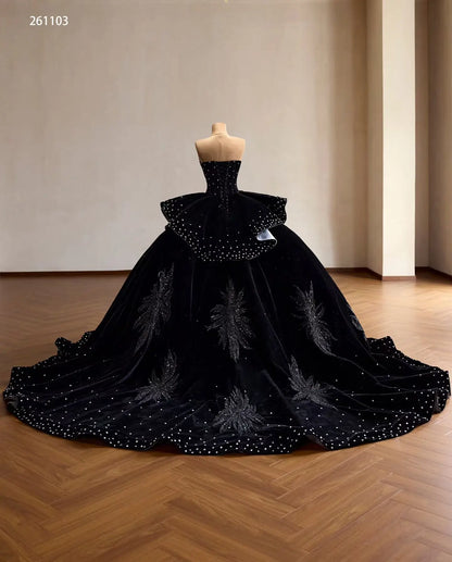 Black velvet quinceañera ball gown with crystal accents, beaded leaf embroidery, ruffle peplum, and a sweeping train.