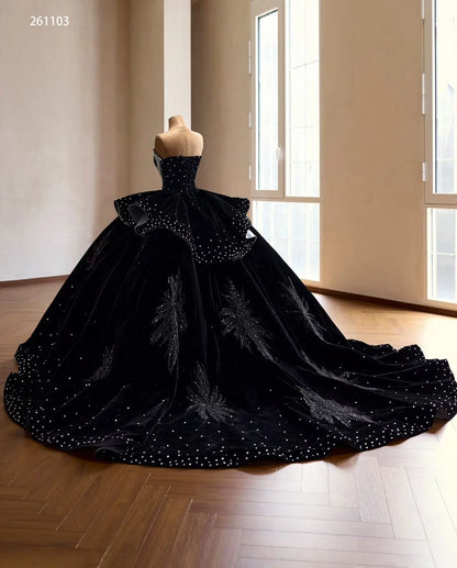 Black velvet quinceañera ball gown with crystal accents, ruffle peplum, and beaded leaf embroidery on a sweeping train.