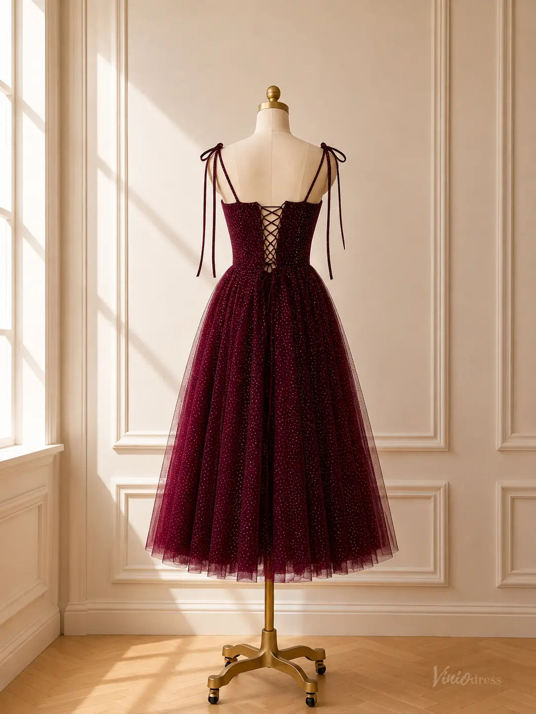 Burgundy tea-length glitter tulle prom dress with tie straps and a lace-up corset back on a mannequin.
