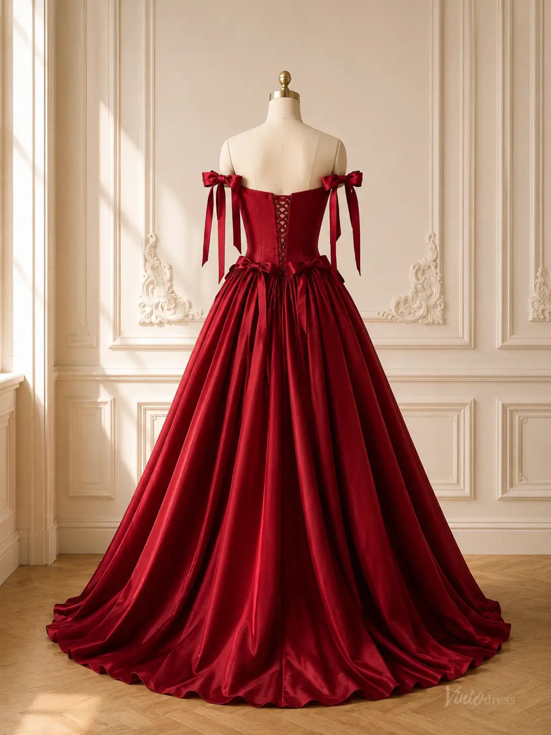 Burgundy satin ball gown with a corset back, basque waist, and off-the-shoulder bow straps on a dress form.