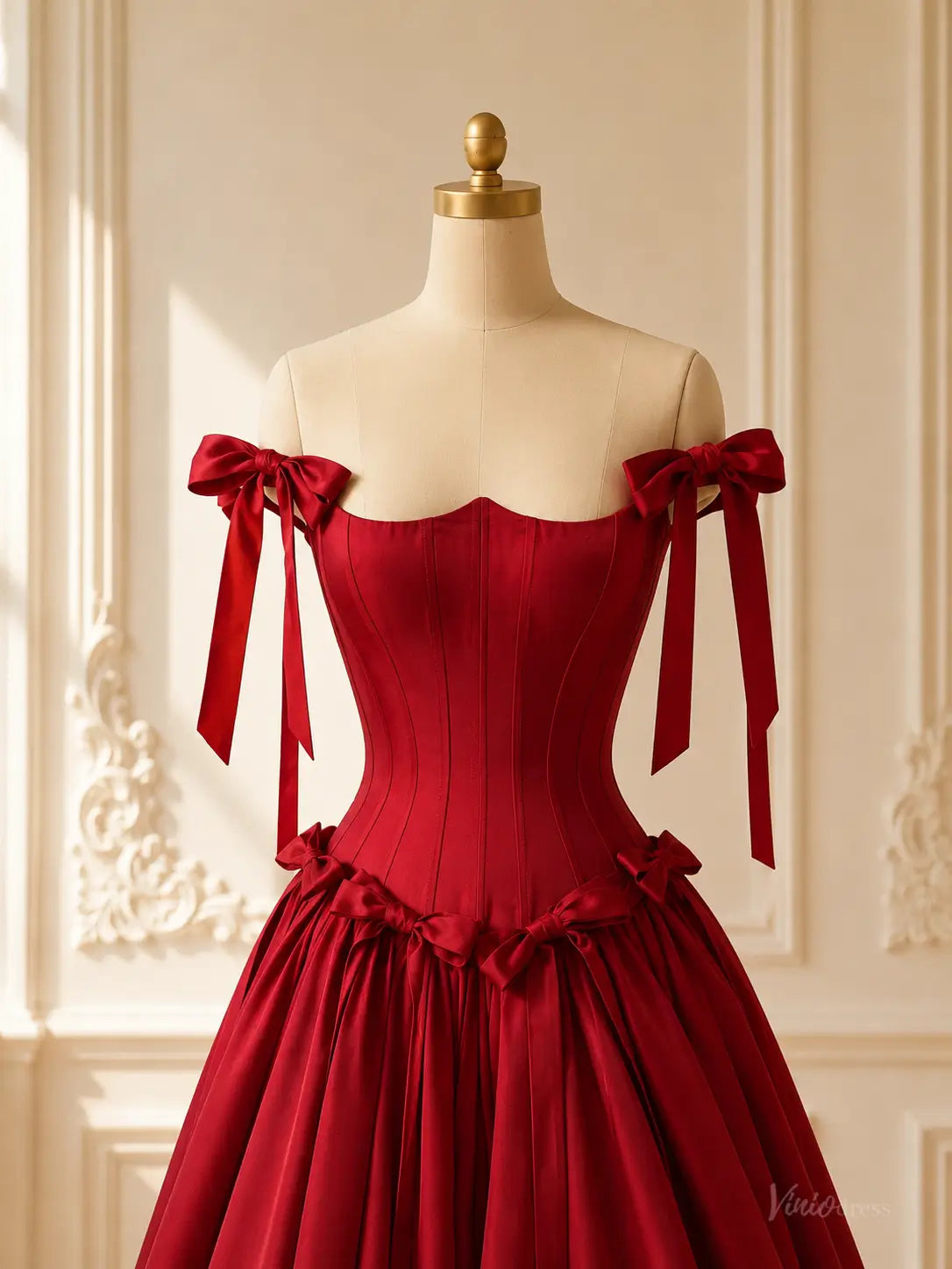 Burgundy satin ball gown with a corset bodice, basque waist, and off-the-shoulder bow straps on a mannequin.