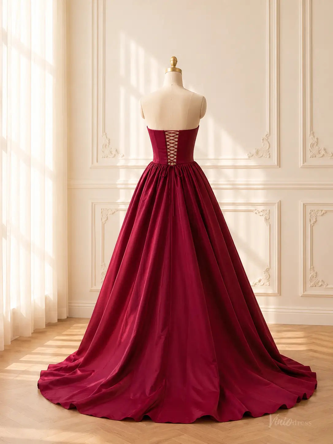 Burgundy satin ball gown with a strapless corset bodice, basque waist, and adjustable lace-up back on a mannequin.