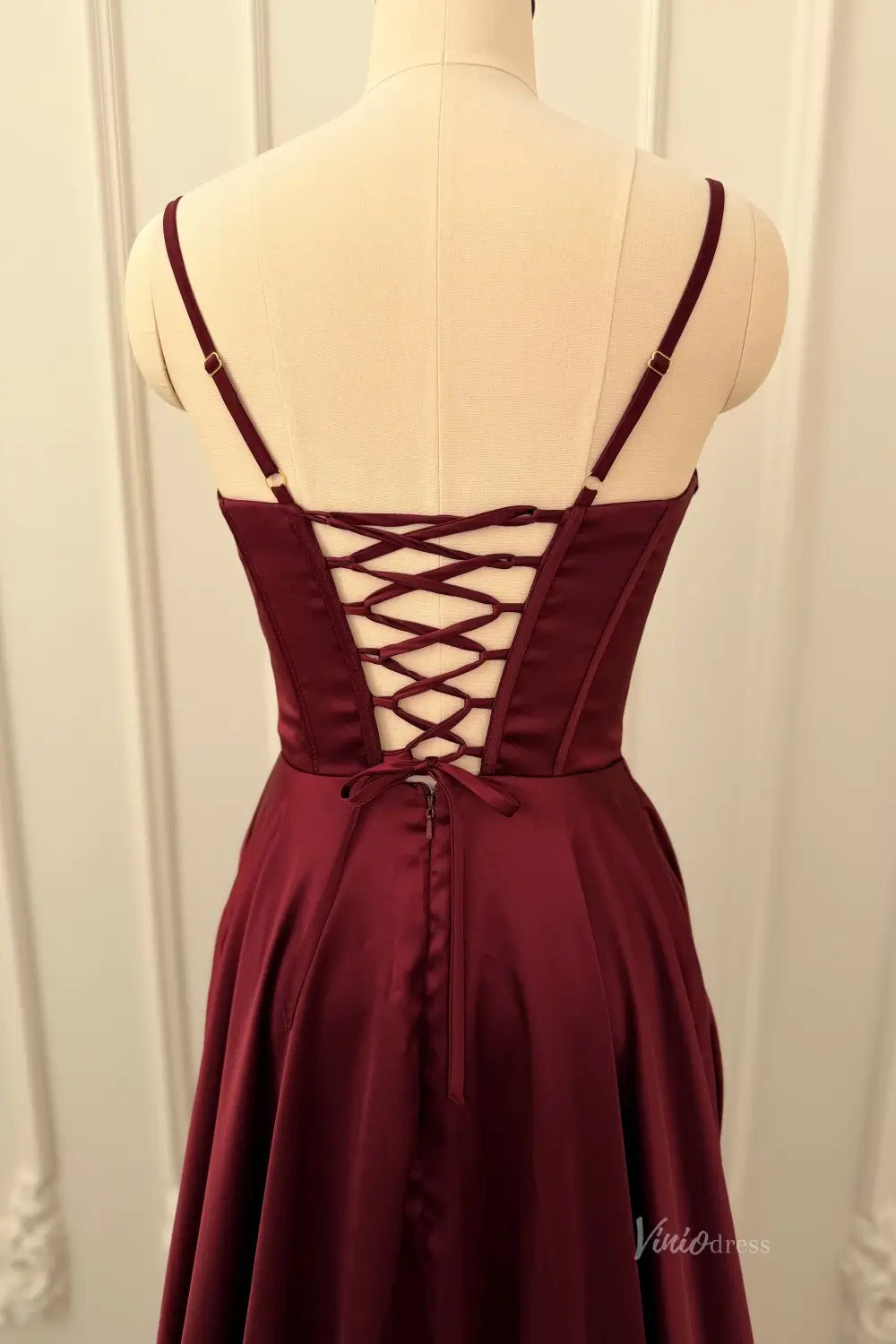 Lace-up back of a burgundy satin prom dress with spaghetti straps on a mannequin.