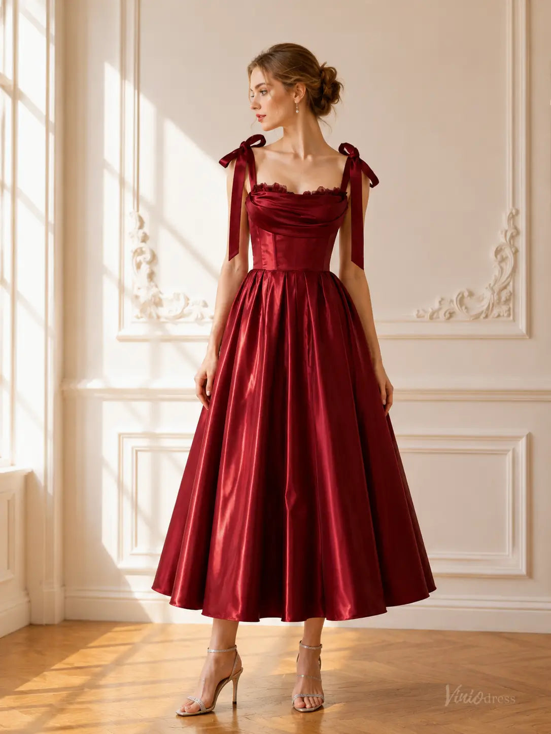 Burgundy satin tea-length prom dress with a corset bodice, draped neckline, and tie bow shoulder straps.
