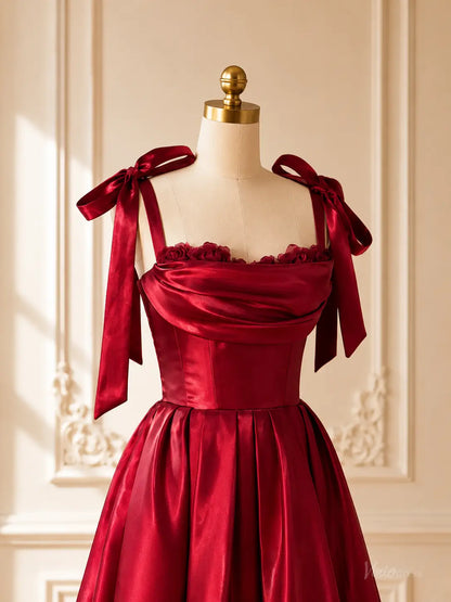 Burgundy satin tea-length prom dress with a corset bodice, draped neckline, 3D floral accents, and tie bow shoulder straps.