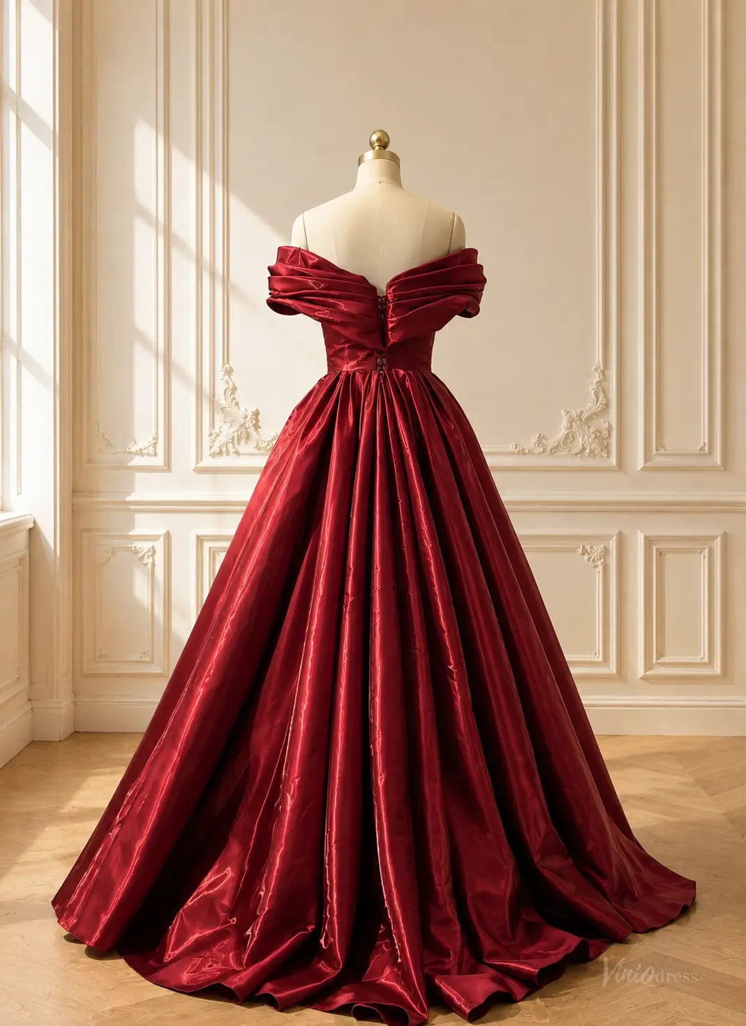 Burgundy satin ball gown with an off-shoulder draped bodice, pleated full skirt, and button-back detail on a mannequin.