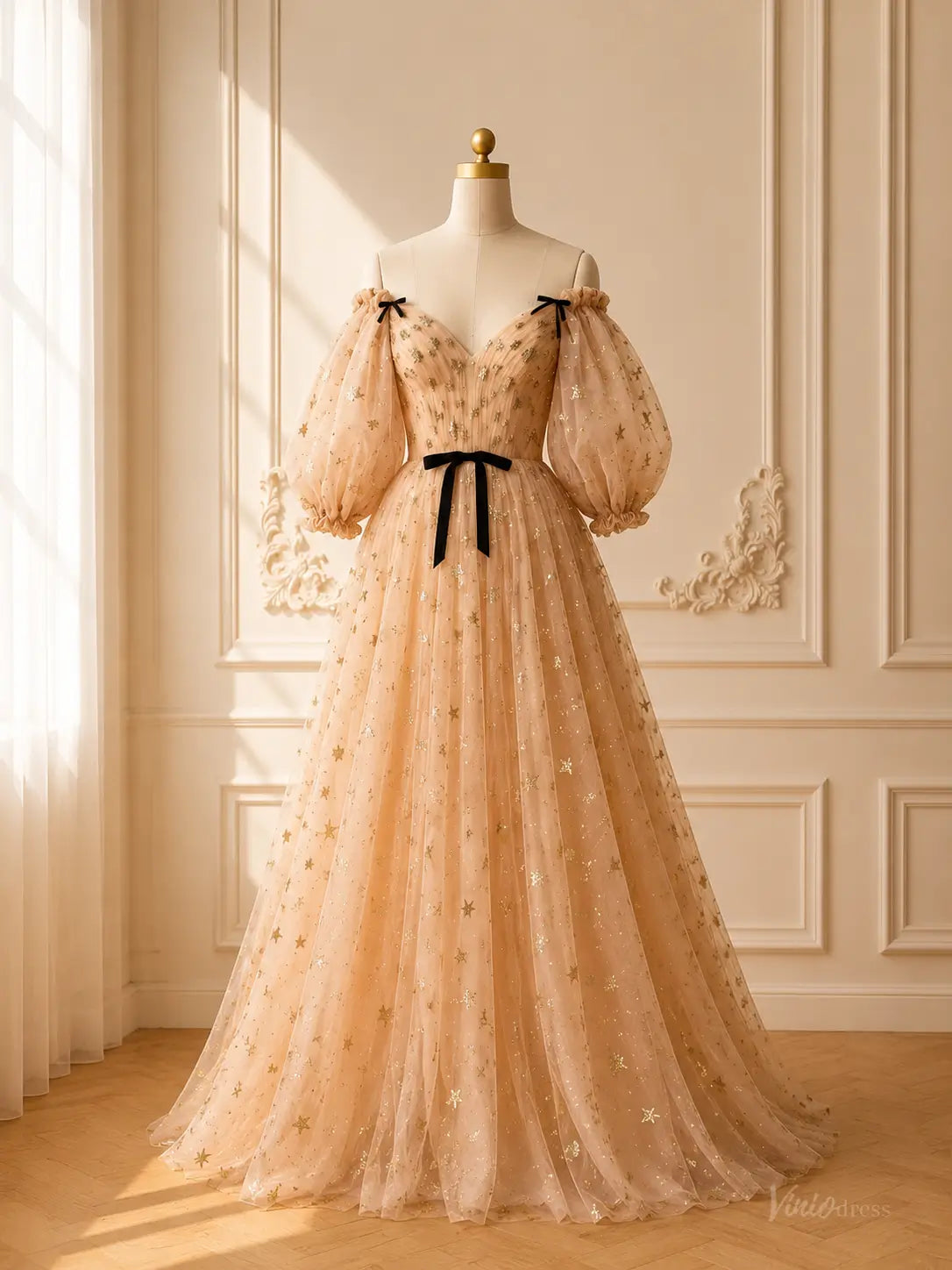 Champagne tulle prom dress with gold stars, puff sleeves, black bow accents, and a sweetheart neckline on a mannequin.