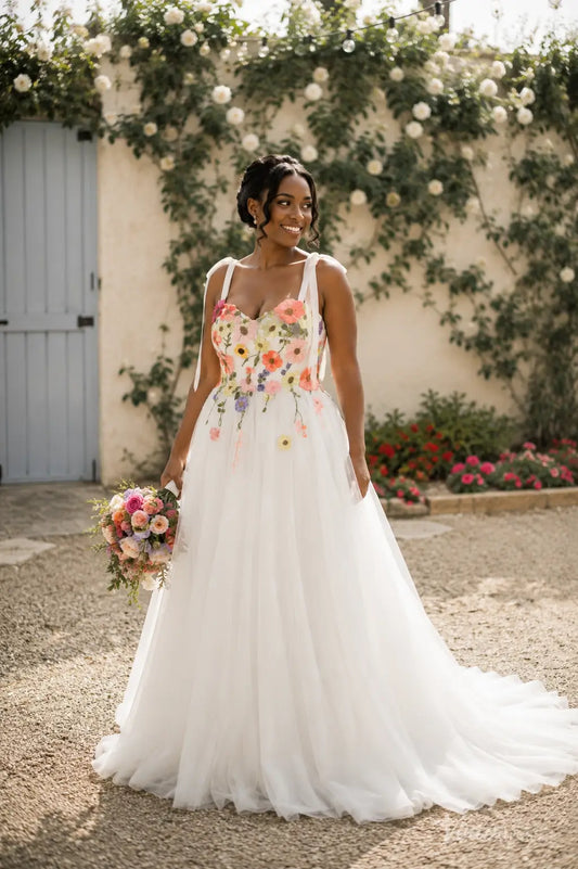 A-line wedding dress with a sweetheart neckline, bow straps, and colorful floral embroidery on an ivory tulle skirt.