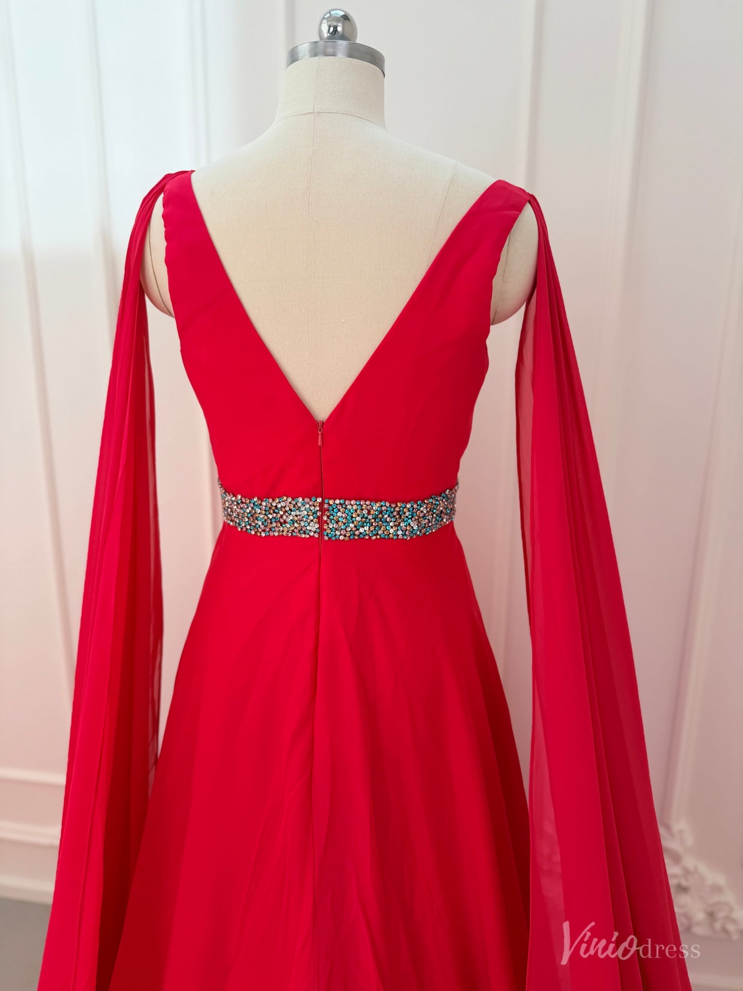 Crimson red chiffon pageant gown with V-neck, dramatic cape sleeves, and a beaded waistline on a dress form.