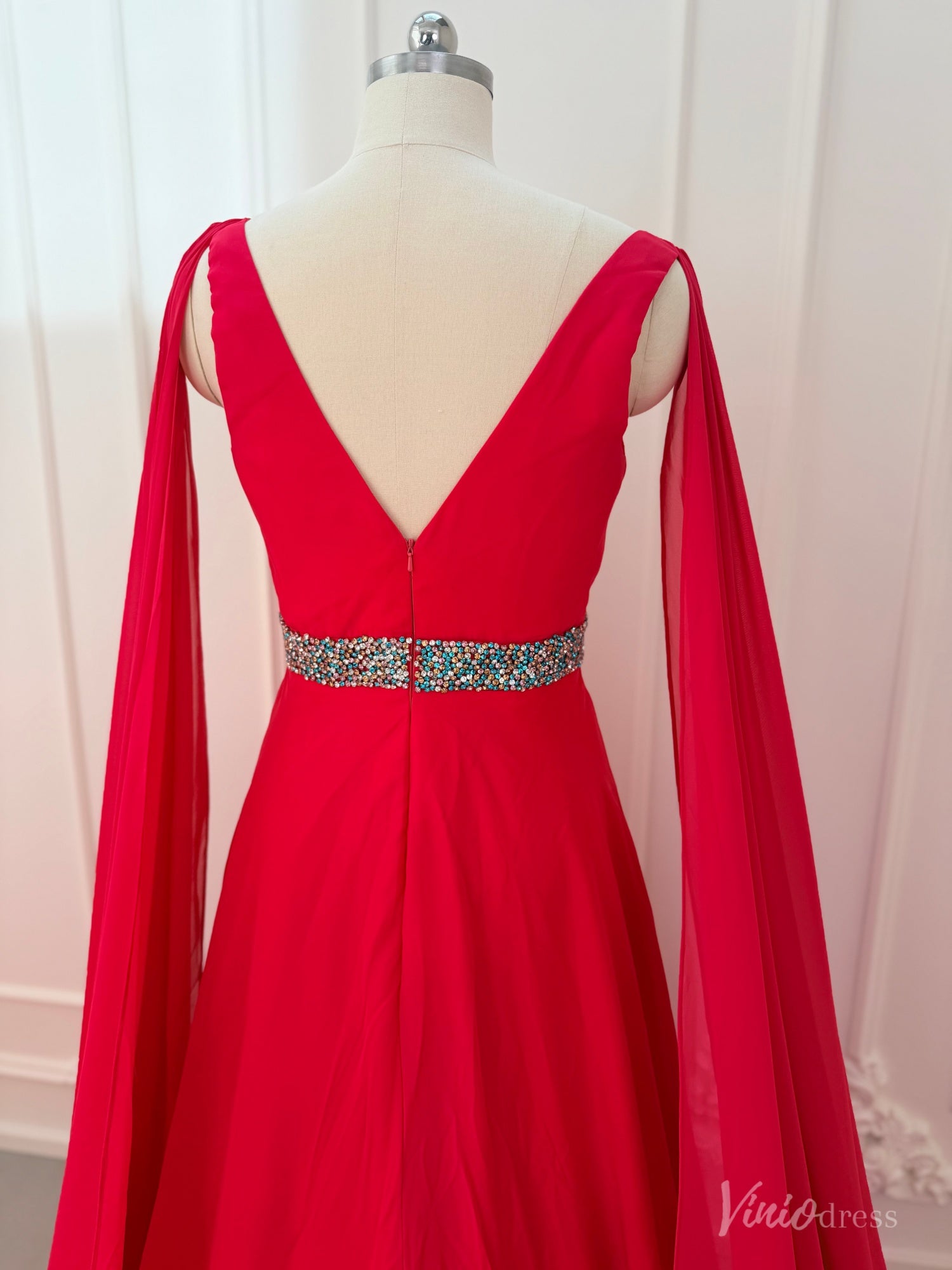 Crimson red chiffon pageant gown with V-neck, dramatic cape sleeves, and a beaded waistline on a dress form.