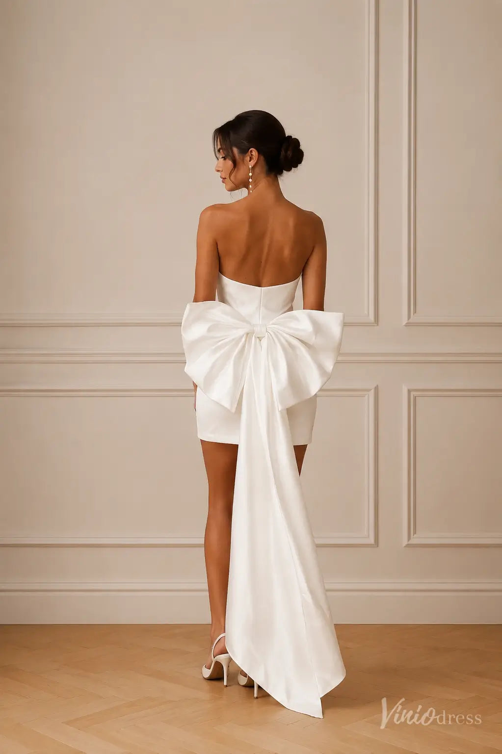 Strapless white satin mini wedding dress featuring an oversized back bow with dramatic floor-length tails.