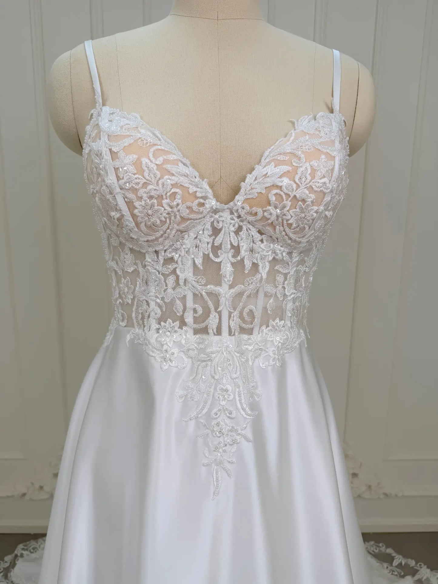White satin wedding dress with a sheer lace appliqué bodice and sweetheart neckline on a mannequin.