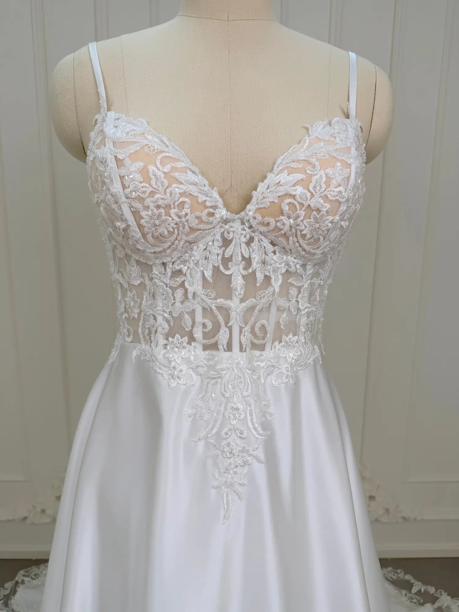 White satin wedding dress with a sheer lace appliqué bodice and sweetheart neckline on a mannequin.