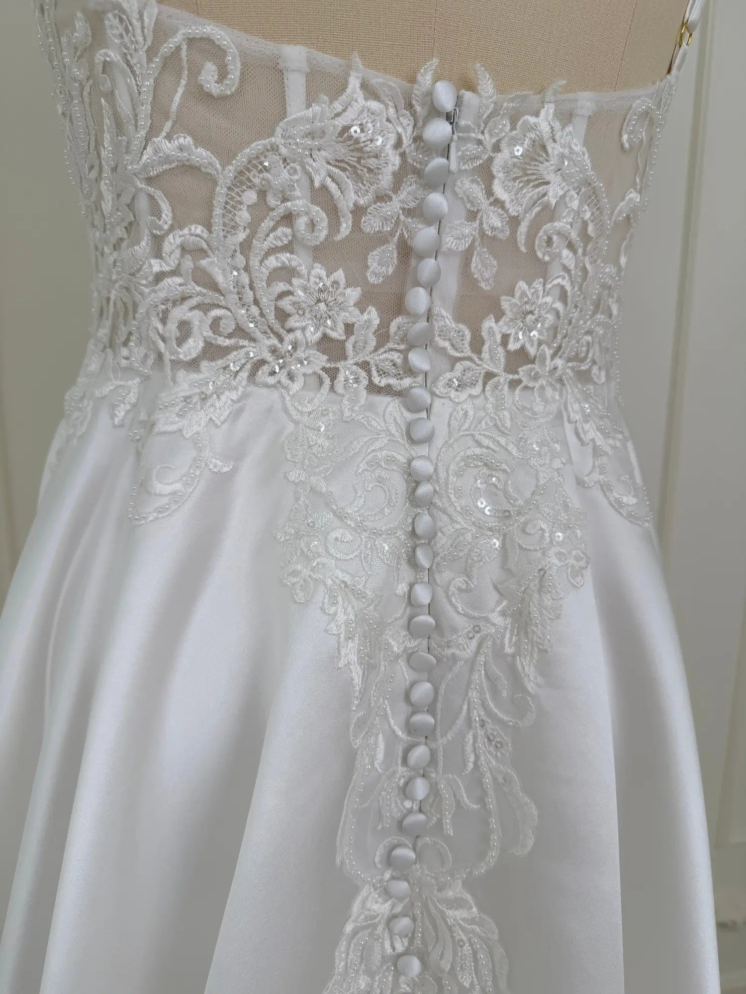 White satin wedding dress back with lace appliqué bodice and covered buttons.
