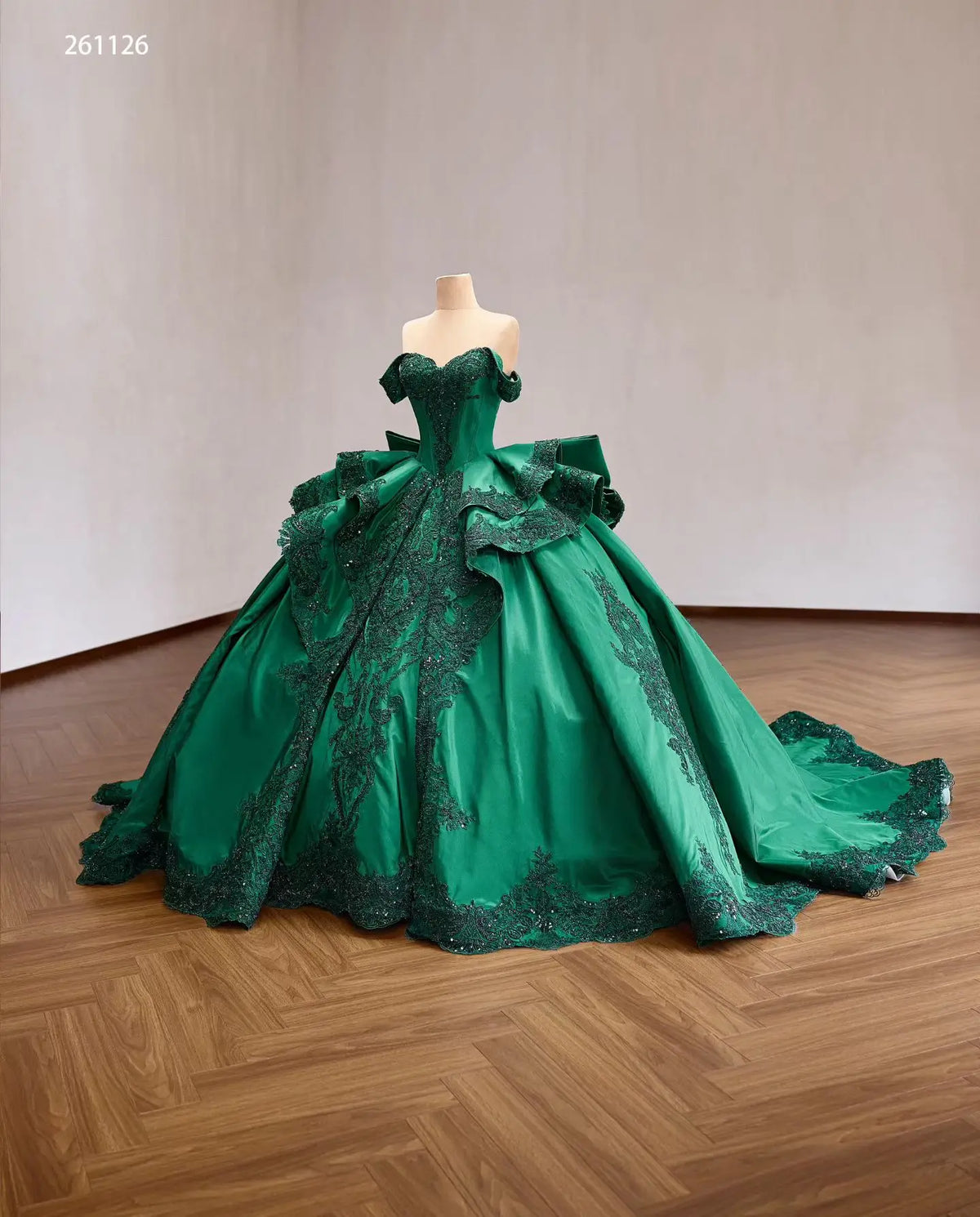 Emerald green quinceañera dress with off-shoulder corset, lace appliqués, layered ruffles, and oversized back bow.