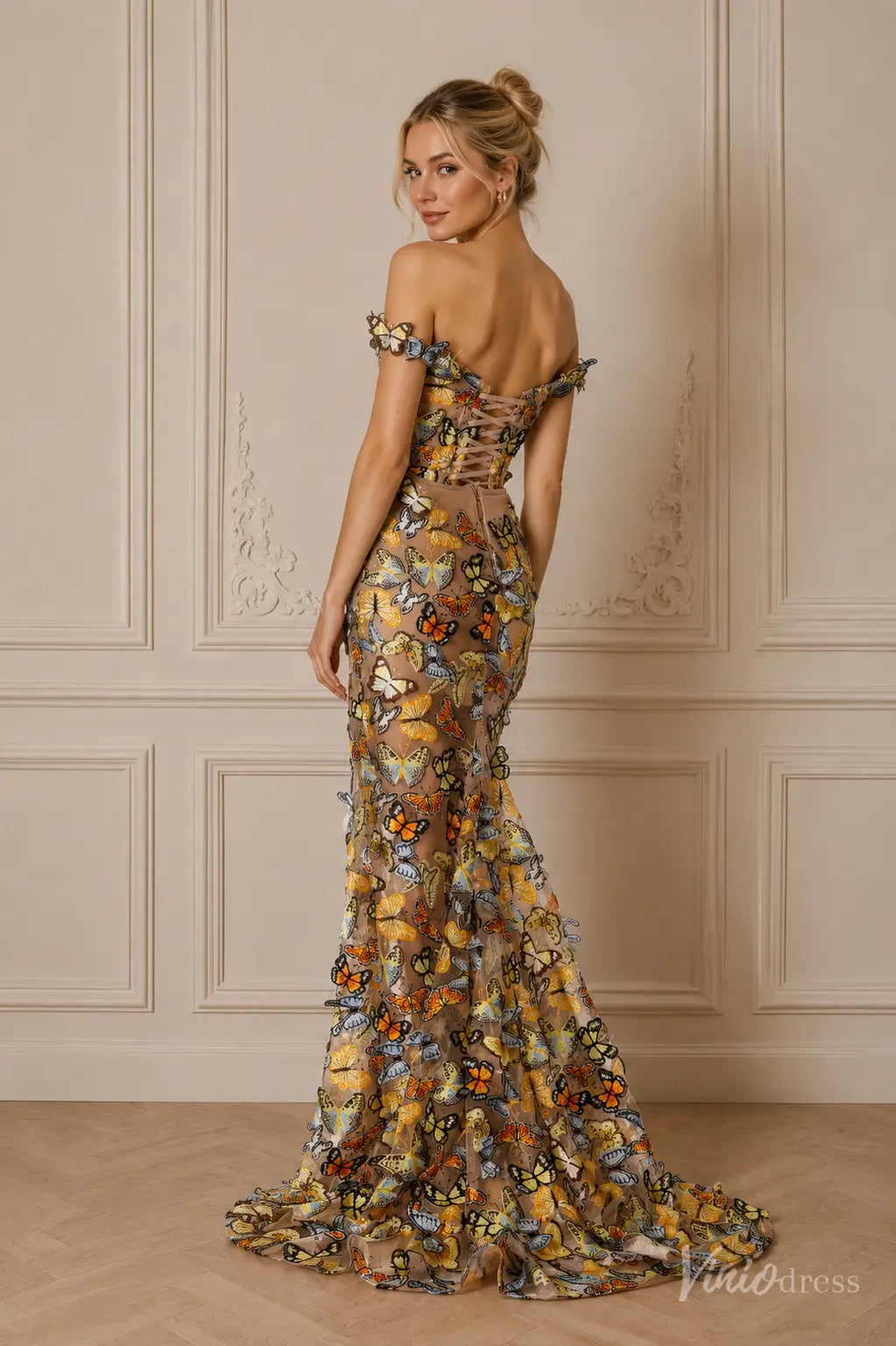 Off-the-shoulder mermaid gown in nude mesh featuring colorful 3D butterfly appliqués and a lace-up corset back.