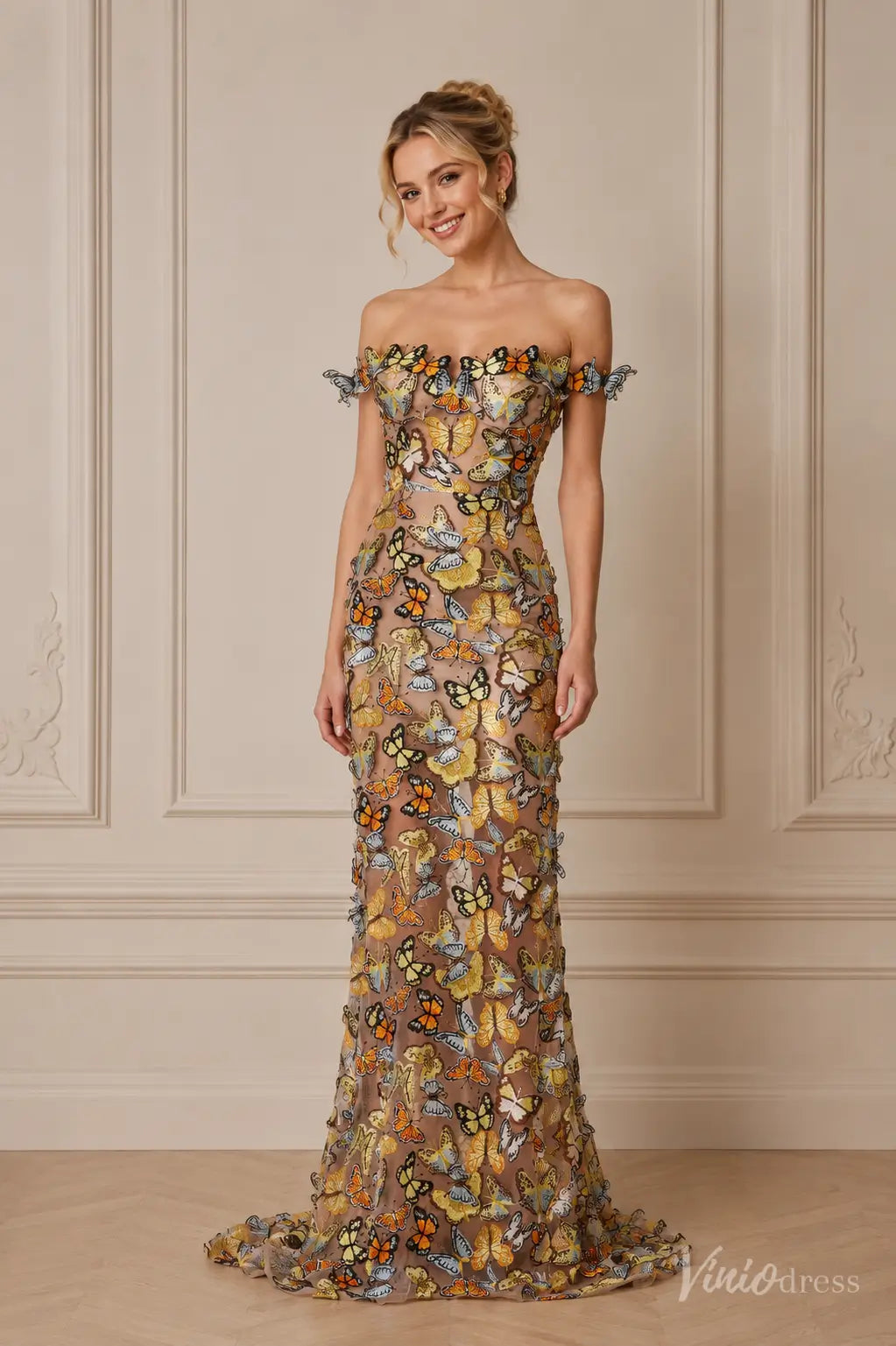 Off-the-shoulder floor-length gown in nude mesh featuring colorful 3D butterfly appliqués and a fitted silhouette.