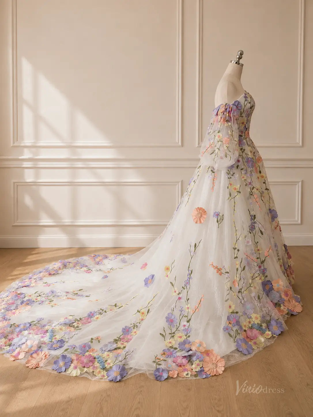 White off-the-shoulder ball gown with a long train, featuring colorful 3D floral embroidery and sheer puff sleeves.