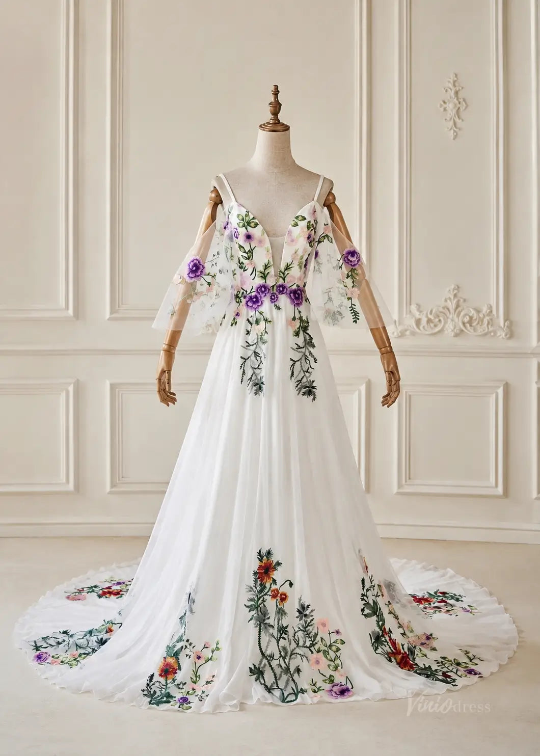 White pleated chiffon gown with colorful floral embroidery, V-neckline, and sheer cold-shoulder sleeves on a mannequin.