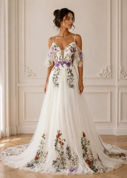 White pleated chiffon wedding dress with cold-shoulder sleeves and colorful floral embroidery throughout the skirt.