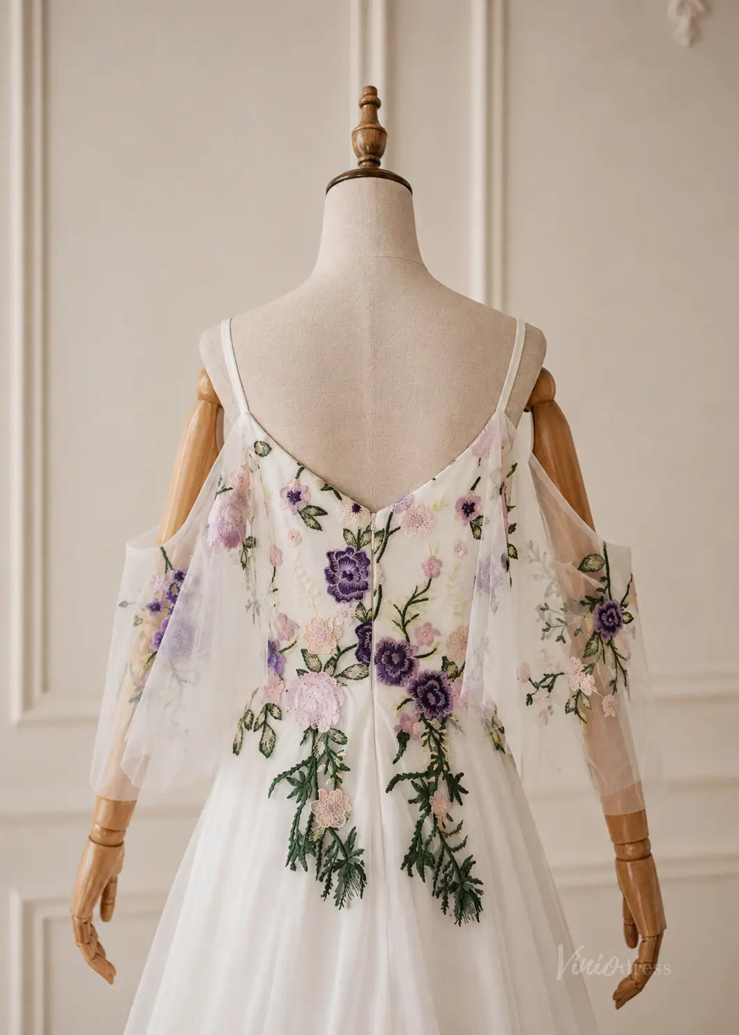 White pleated chiffon dress with cold-shoulder sleeves and colorful floral embroidery on a mannequin.