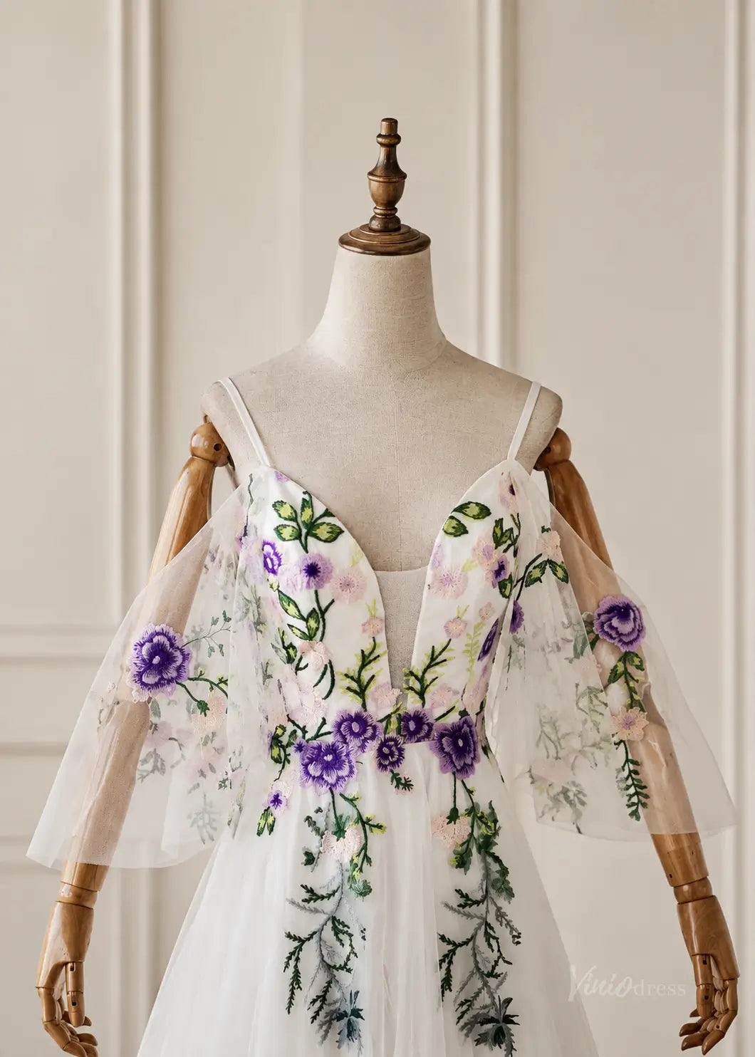 White pleated chiffon dress with purple and green floral embroidery, featuring a deep V-neck and sheer off-shoulder sleeves.