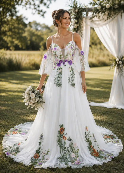 White pleated chiffon wedding dress with cold-shoulder sleeves and colorful floral embroidery in a garden setting.