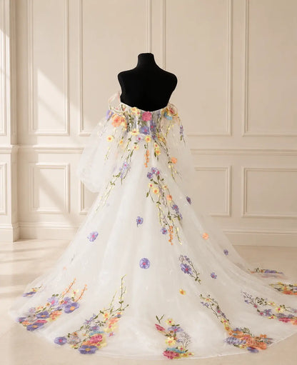 Off-the-shoulder white wedding dress with sheer puff sleeves and colorful floral embroidery on a flowing tulle skirt.