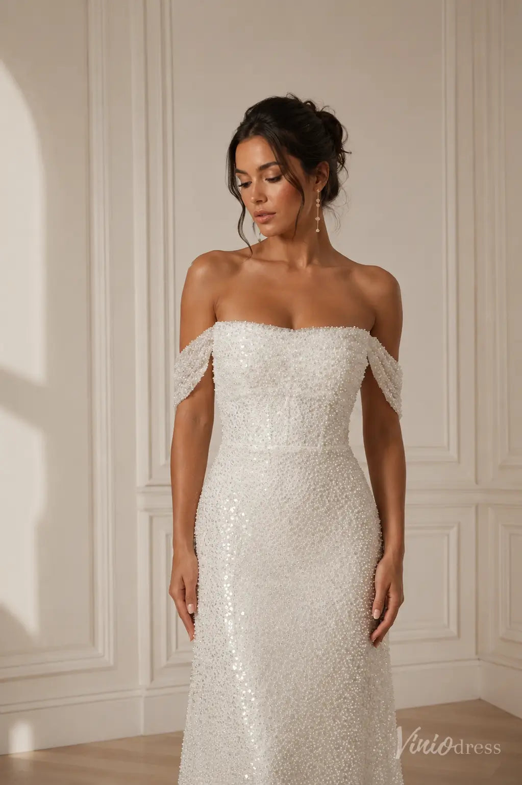 Off-the-shoulder white wedding dress featuring intricate pearl and sequin embellishments on a fitted bodice.